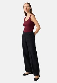 Bordeaux geribbelde tanktop gecombineerd met hooghangende zwarte wijde broek en zwarte flats; gladde stoftextuur met een minimalistisch ontwerp.