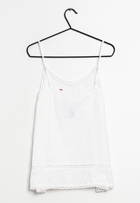 Bílý bavlněný tílko s tenkými ramínky, se krajkovým lemem podél spodního okraje a malým červeným akcentem u oblasti poprsí.