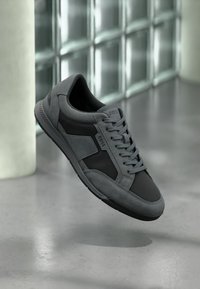 Baskets grises en cuir et suède, avec un design à lacets, des accents texturés et un bout rond. Semelle extérieure fine en caoutchouc visible.