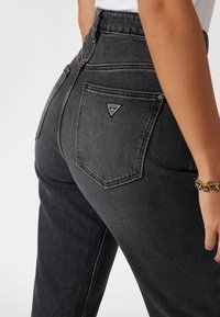 Jeans de mezclilla negros de cintura alta con una textura suave. Presentan un logotipo triangular en el bolsillo trasero y costuras en contraste.