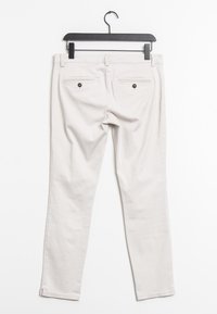 Pantalon blanc en coton à coupe slim, avec deux poches arrière ornées de boutons noirs et une coupe droite. Suspendu sur un cintre noir.