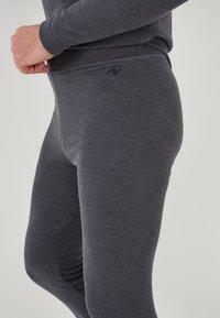 Leggings grises hechos de una tela suave y elástica. Presentan una cintura alta y un sutil detalle del logo, con una textura suave y mate.