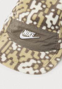 Cască Nike din fleece moale, cu model, în nuanțe de bej, crem și maro, cu o etichetă din nailon bej și logo brodat pe față.