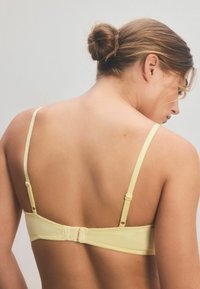 Sutien galben cu bretele ajustabile, închidere cu cârlig și ochi la spate și material neted, fără modele sau embellishments vizibile.