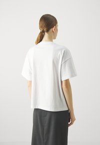 Camiseta de algodón blanca con mangas cortas, corte relajado y escote redondo; el dobladillo está ligeramente curvado en la parte posterior.