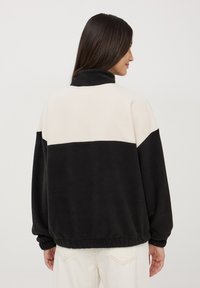 Giacca in pile color block nera e crema con colletto alto e orlo elastico. Presenta maniche ampie e una texture morbida.