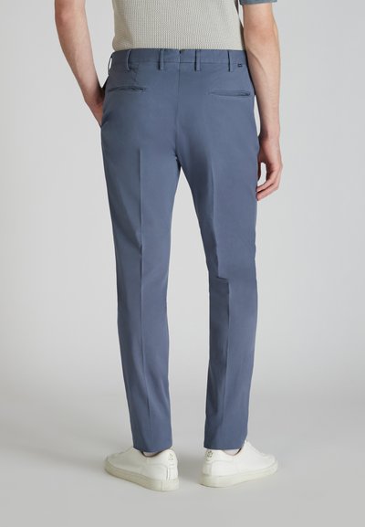 Herren Slim-Fit-Hose aus dunkelblauem Stoff, mit zwei Gesäßtaschen und glatter Textur. Getragen mit weißen Sneakers.