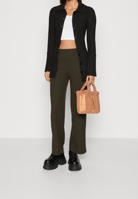 Kvinna iklädd en svart knappad cardigan, vit kortärmad topp, olivgröna ribbade byxor, svarta platåskor och håller en beige teddyhandväska.