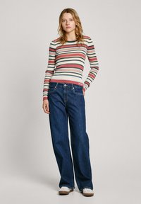 Gestreepte langekavec shirt in pastelkleuren, gecombineerd met losse donkerdenim jeans. Casual sportschoenen en een minimalistisch ontwerp.