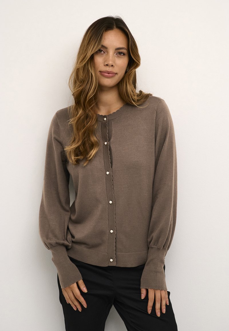 Cauri brūns džemperis, izgatavots no mīksta materiāla, ar apaļu kaklu, pūkainām piedurknēm un pogu aizdari ar ielaistām malām un pērļu pogām.