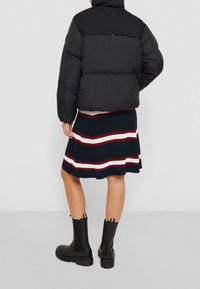 Chaqueta acolchada negra con cuello alto, combinada con una falda de canalé azul marino con rayas rojas y blancas, y botines negros con suela texturizada.