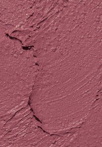 Krämig läppstift i en mauve nyans, med en slät textur och lätt lyster. Ytan visar ojämn applicering med streck och sprickor.