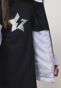 Top negro con un diseño de estrella plateada, que presenta acentos de tachuelas y una chaqueta suave y negra de pelaje con forro blanco y mangas anchas.