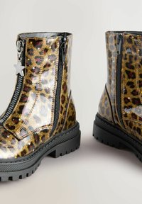 Glänzende Ankle Boots mit Leopardenmuster in Gold- und Schwarztönen, ausgestattet mit doppelten Reißverschlüssen, einer strukturierten Sohle und einem schwarzen Sternanhänger.