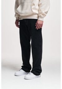 Czarne dżinsy z denimu o luźnym kroju, zestawione z białymi trampkami. Strój uzupełnia kremowa bluza z kapturem z detalem w postaci przedniej kieszeni.