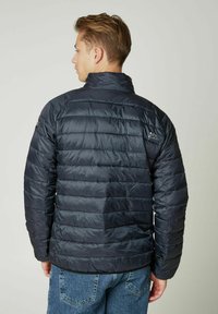 Juosmens juodas pamušalas su aukštu apykakle, su horizontaliomis siūlėmis ir logotipo detale ant peties. Dėvima ant atsitiktinių džinsų.