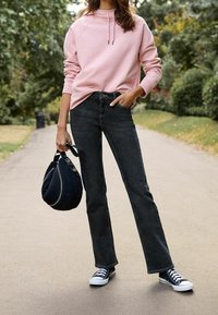 Jasnoróżowa bluza z kapturem, czarne obcisłe jeansy, czarne trampki oraz ciemnoniebieska torba z srebrnymi akcentami, noszone na ścieżce z zielonym tłem.