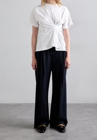 Bílý krátký rukáv top s detailem twist na přední straně, spárovaný s námořnickými širokými kalhotami a černými botami se zlatým akcentem.