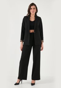 Black tailored blazer with a single button, wide-leg black trousers, and a black crop top. Notable leopard print detail on the blazer cuffs.