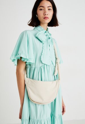 Kremfarget håndveske med en buet form, myk tekstur og justerbar stropp, båret over en lys mintgrønn rynket kjole.