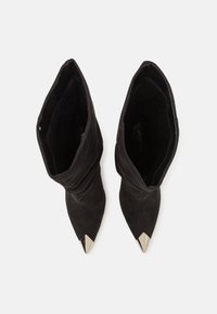 Botas de tobillo de ante negro con un diseño holgado y puntas afiladas. Presentan detalles metálicos puntiagudos en las punteras.