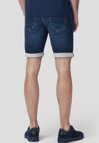 Ciemnoniebieskie szorty dżinsowe z podwiniętymi mankietami, z pięcioma kieszeniami i kontrastowym szwem, w zestawieniu z ciemnymi sneakerami.