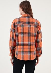 Narancssárga kockás flaneling fekete és navy mintákkal, galléros nyakkal és gombos mandzsettával. Puha textúra, laza fazon.