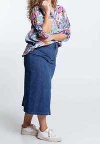 Chemise à boutons avec impression florale et manches retroussées ; coupe décontractée. Jupe midi en denim bleu foncé ; fentes sur les côtés. Baskets de sport blanches.