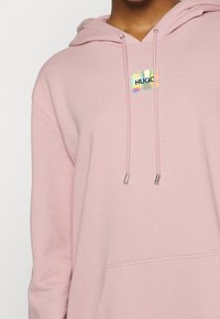 Rosa Kapuzenpullover aus weichem Stoff, mit einer vorderen Kängurutasche, Zugbändern mit metallischen Spitzen und einem holografischen Markenlogo-Patch.