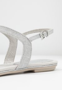 Hopeat teksturoidut sandaalit, joissa on litteä pohja, kaksi remmiä ja säädettävä nilkkahihna. Pehmeä mokkanahkainen pohja.
