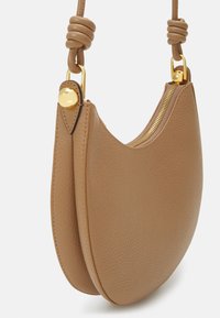 Borsa a forma di mezzaluna in pelle color tan con zip dorata, dettaglio della tracolla annodata e bordi arrotondati. La superficie testurizzata aggiunge tridimensionalità.