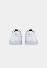 Paire de baskets blanches décontractées avec un logo crocodile gris à l'arrière, vue de dos sur un fond uni.