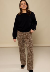 Zwarte sweatshirt met een ronde hals en omgeplooide mouwen, gecombineerd met lichtbruine broek met luipaardprint en wijde pijpen, en zwarte plateauschoenen.