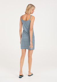 Blaues gemustertes Kleid mit dünnen Trägern, das ein geometrisches Design und eine taillierte Form aufweist. Kombiniert mit einfachen Flip-Flops. Glatte Textur.
