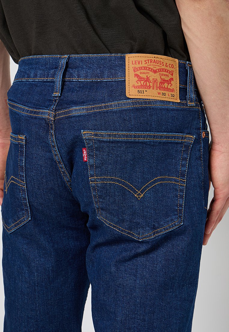 Dark blue denim jeans with a slim fit, featuring contrasting yellow stitching, a leather logo patch, and classic back pocket designs.