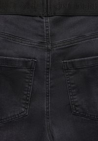 Svarta denimjeans med en slät textur, med två bakfickor, vertikala sömmar och en midja med präglad text.