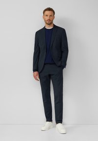 Granatowy garnitur z dopasowanymi spodniami i granatowym swetrem pod spodem, połączony z białymi sneakerami. Gładki materiał, slim fit, minimalistyczny design.