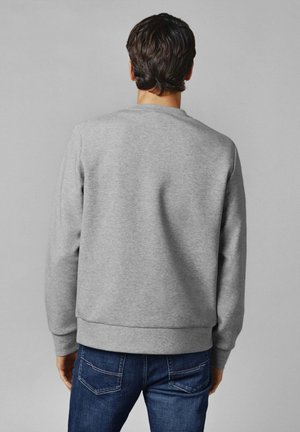 Šedá mikina s kulatým výstřihem, vyrobená z měkké tkaniny. Má žebrované manžety a lem, doplněná modrými džínami.