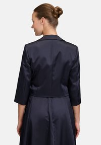 Granatowa satynowa kurtka o dopasowanym kroju, z rękawami o długości trzech czwartych i klasycznym kołnierzykiem, prezentowana z tyłu, podkreślająca jej gładką fakturę.