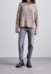 Suéter de punto en hilo multicolor, con cuello alto y ajuste holgado, combinado con jeans rectos gris claro y botas de tobillo negras.