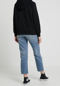 Felpa nera con cappuccio, jeans cropped azzurri, e sneakers nere alte con dettagli bianchi; un look casual con vestibilità rilassata.