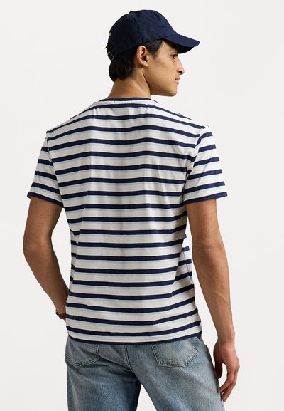 Randig t-shirt i vitt och marinblått, kortärmad, med rund halsringning. Bärs med blå jeans som har en avslappnad passform och subtil textur.