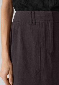 Jupe en lin violet foncé avec une taille ajustée, des passants de ceinture et des poches latérales. Le tissu a une finition texturée et un éclat subtil.