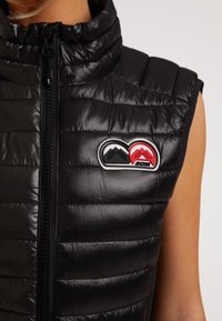 Schwarze ärmellose Daunenweste mit hohem Kragen, glänzender Textur, vertikal gestepptem Muster und einem bunten Doppelberg-Logopatch.