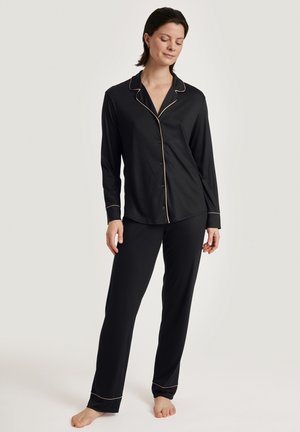 Zwarte pyjama set met een langelijnafgeknopte top en rechte broekspijpen. Gouden piping accenten op de kraag, manchetten en zoom. Zacht textuur van de stof.