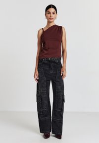 Top asimmetrico color marrone scuro con dettaglio drappeggiato, abbinato a pantaloni cargo neri a vita alta con tasche laterali e cuciture a contrasto.