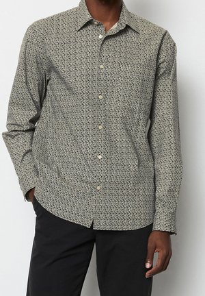 Camicia a maniche lunghe beige chiaro con un motivo scuro. Presenta un colletto classico, chiusura con bottoni e una vestibilità rilassata. Tessuto testurizzato.