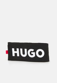 Black fabric band with bold white "HUGO" text. Features a textured surface and a red accent tag on one side. Simple rectangular design.