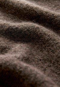 Hnědá textilie s texturovaným, měkkým povrchem, zobrazující mírně chlupatý, tkaný vzor. Barevné variace vytvářejí hloubku a teplo.