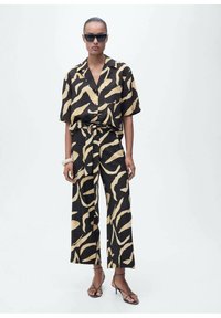 Ensemble bi-matière noir et or avec un haut à manches courtes et une fermeture à boutons, accompagné d'un pantalon large, le tout en matériau léger.